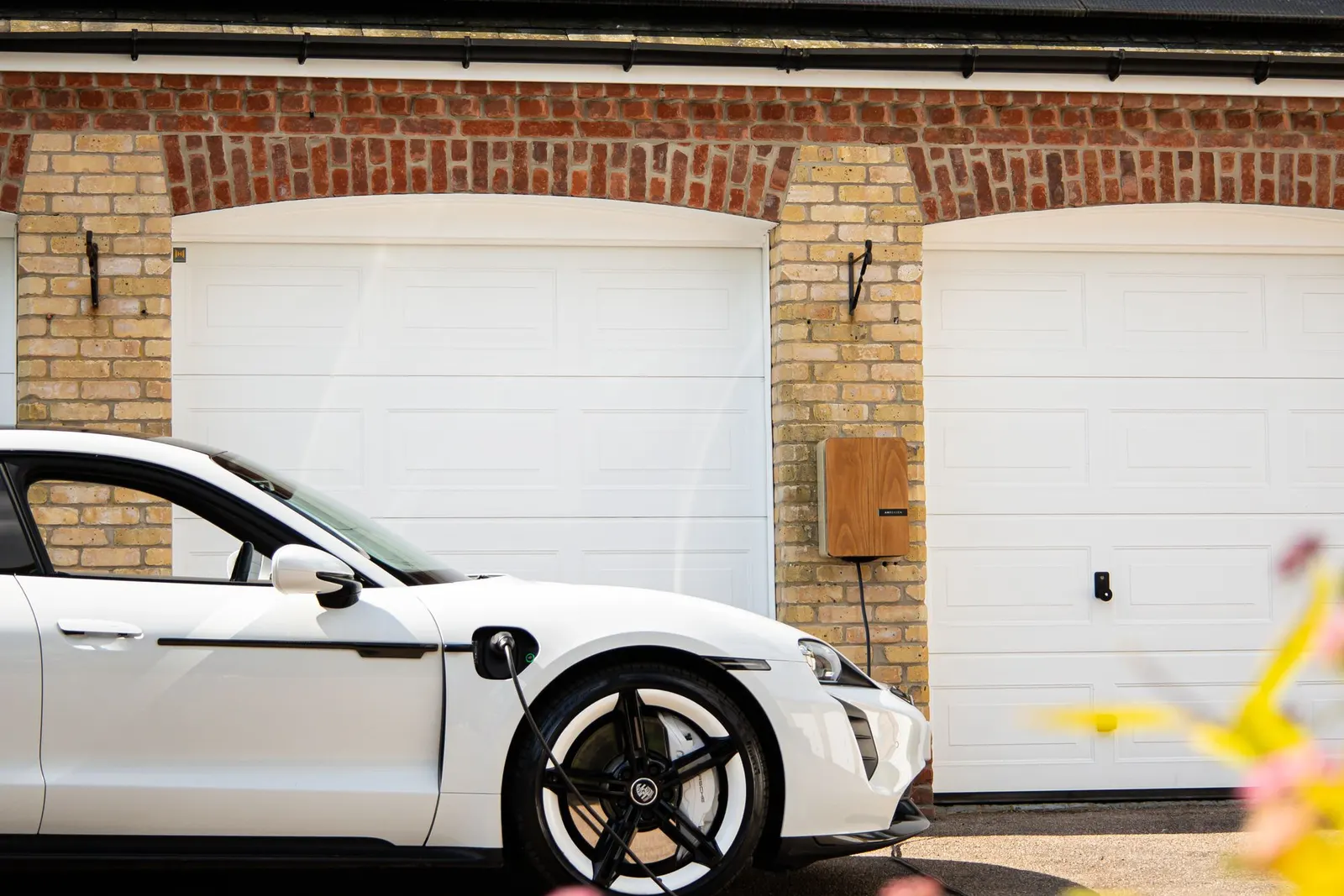 Weißes Elektroauto vor einer Doppelgarage mit Wallbox an der Hauswand