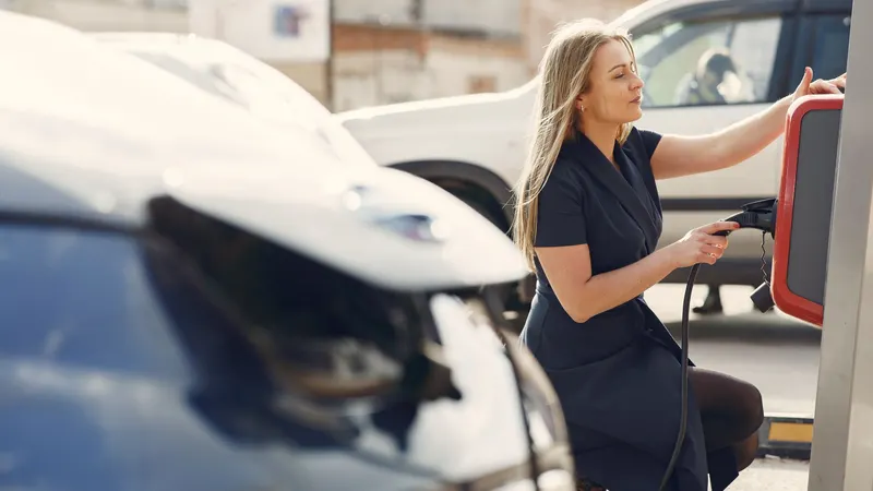 Frau steckt an einer Ladesäule auf einem Parkplatz das Ladekabel in ein Elektroauto